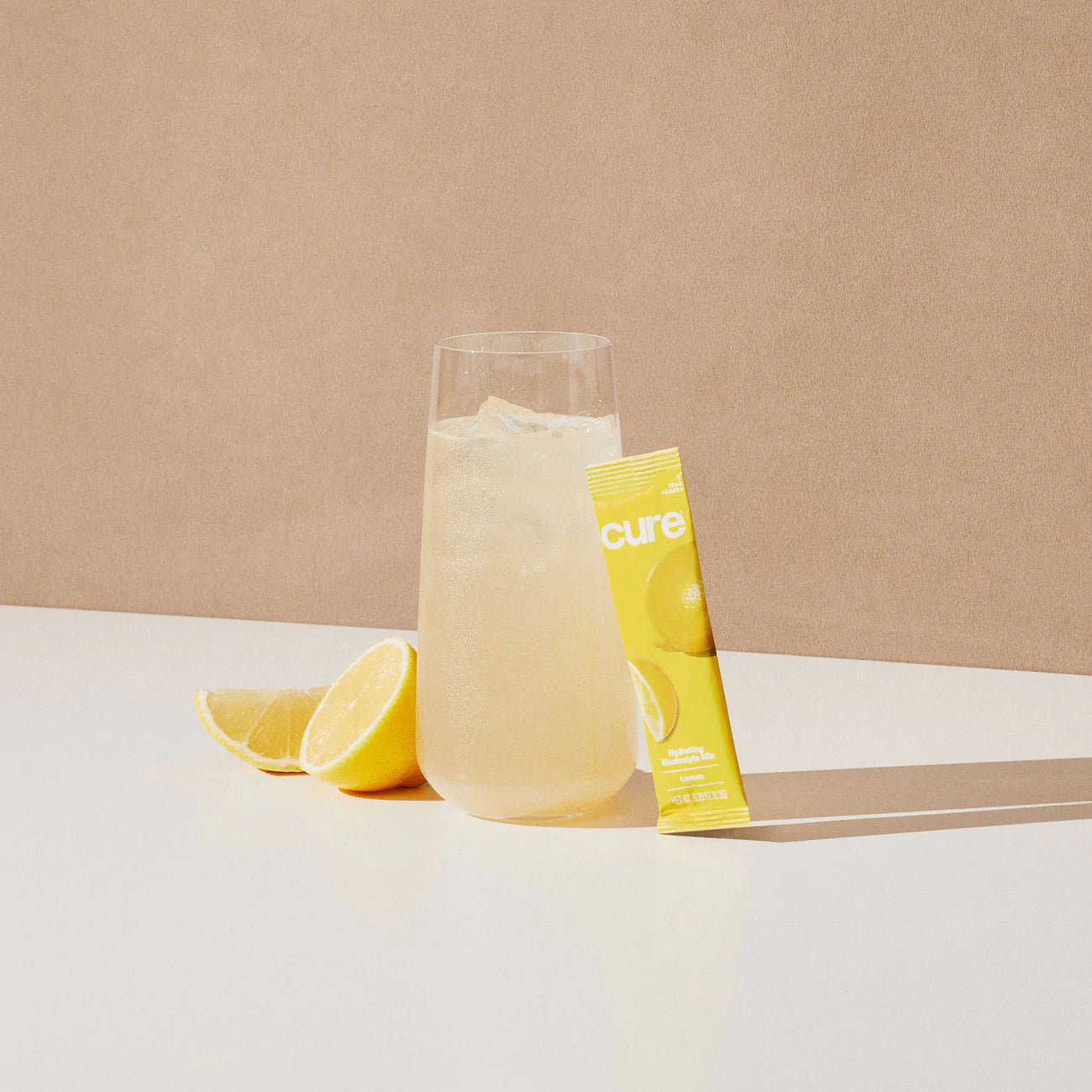 Glass of lemonade with ice, lemon wedge, and yellow 'cure' packet labeled 'Berry Pomegranate/Lemonade Bundle'