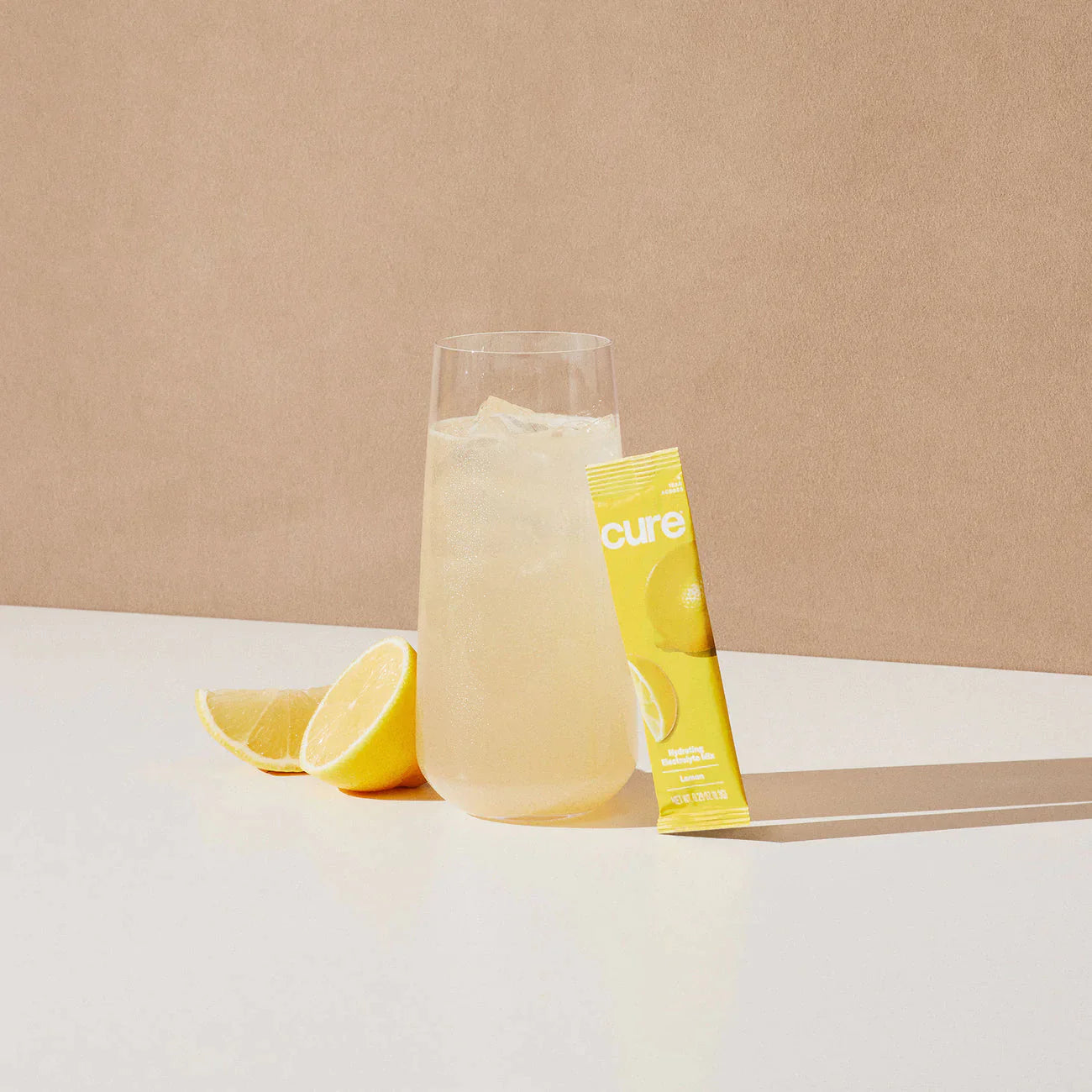 Glass of lemonade with ice, lemon halves, and a yellow packet labeled 'cure'