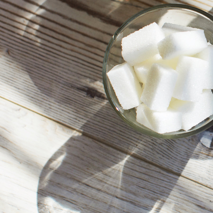 Glass bowl filled with white sugar cubes on a wooden table casting shadows