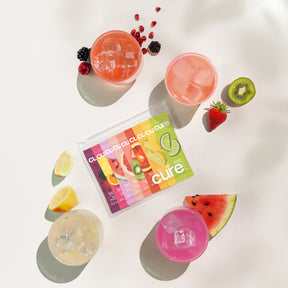 Four colorful drinks with ice, assorted fruit slices (lemon, kiwi, strawberry, watermelon, berries), and a Cure Starter Kit pack with fruit-flavored sachets.