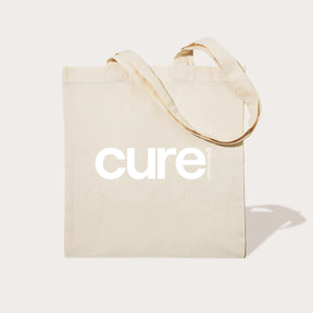 Beige tote bag with the word 'cure' printed in large white letters on the front.
