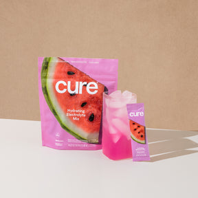 Hydrating Electrolyte Mix 'cure' Watermelon flavor package with a glass of pink drink and a single serving stick