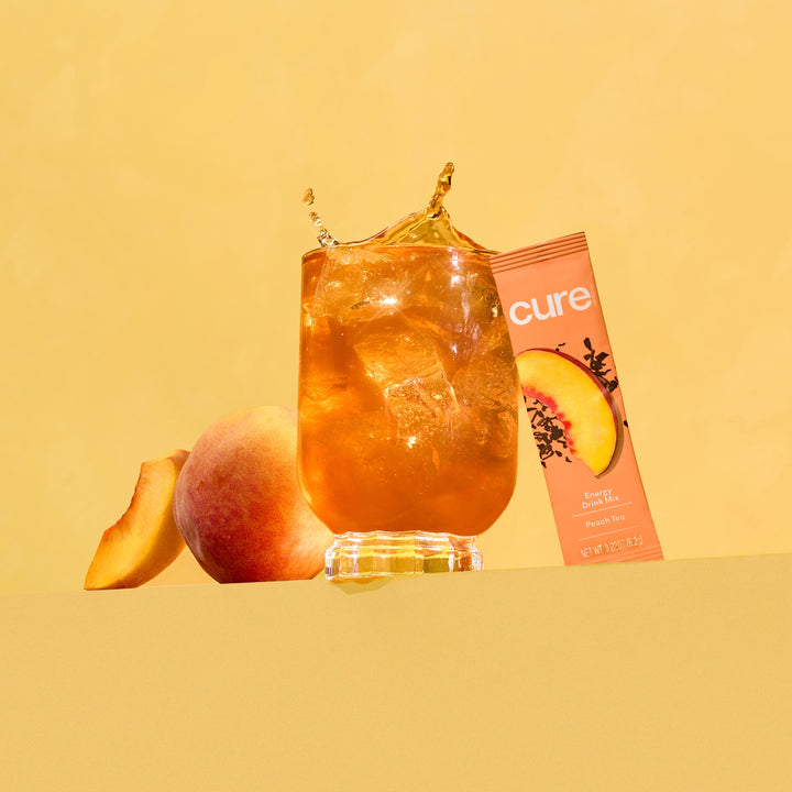 Iced peach drink with splash, peach fruit, and 'cure' peach variety pack packaging on yellow background