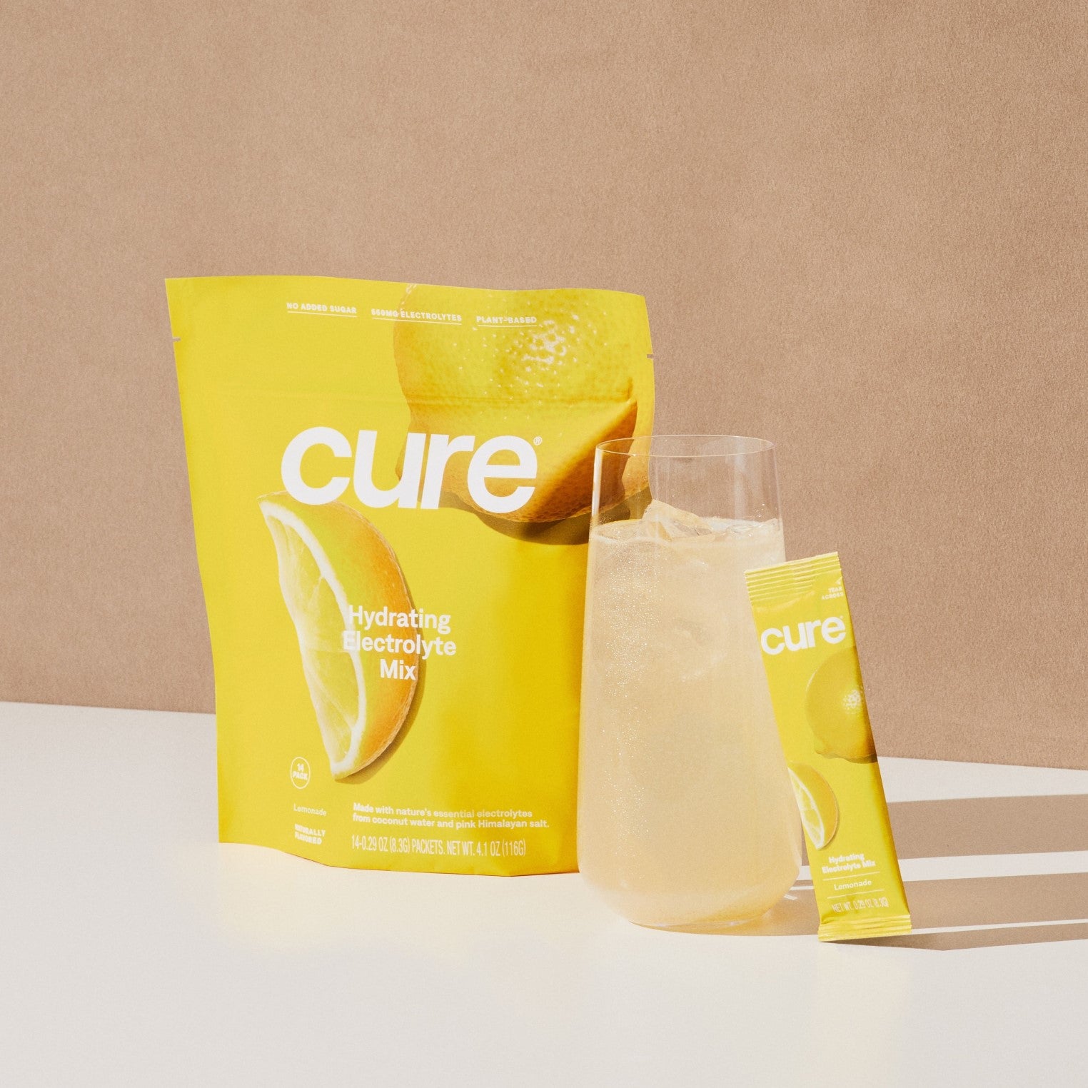 Yellow 'cure hydrating electrolyte mix' packet with lemon slice image, a glass of lemonade, and a single stick pack labeled 'cure'