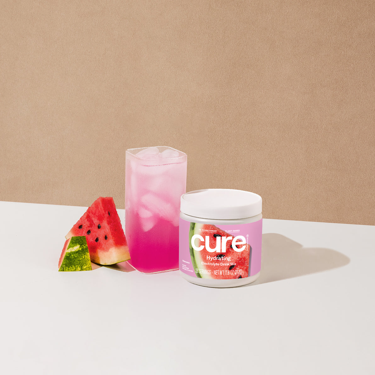 Jar labeled 'cure watermelon' next to a pink iced drink and two watermelon slices on a white surface.
