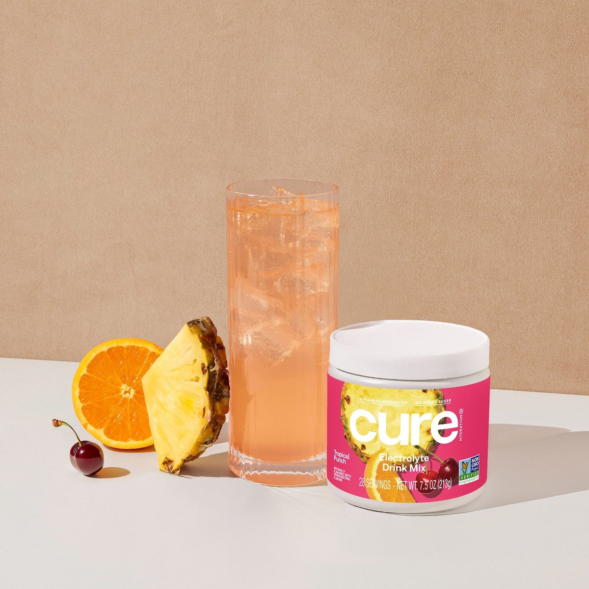 Glass of tropical punch drink with ice, pineapple slice, orange half, cherry, and a jar labeled 'cure' Tropical Punch Bulk Jar