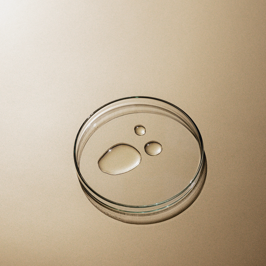 Petri dish with three water droplets on a beige surface.